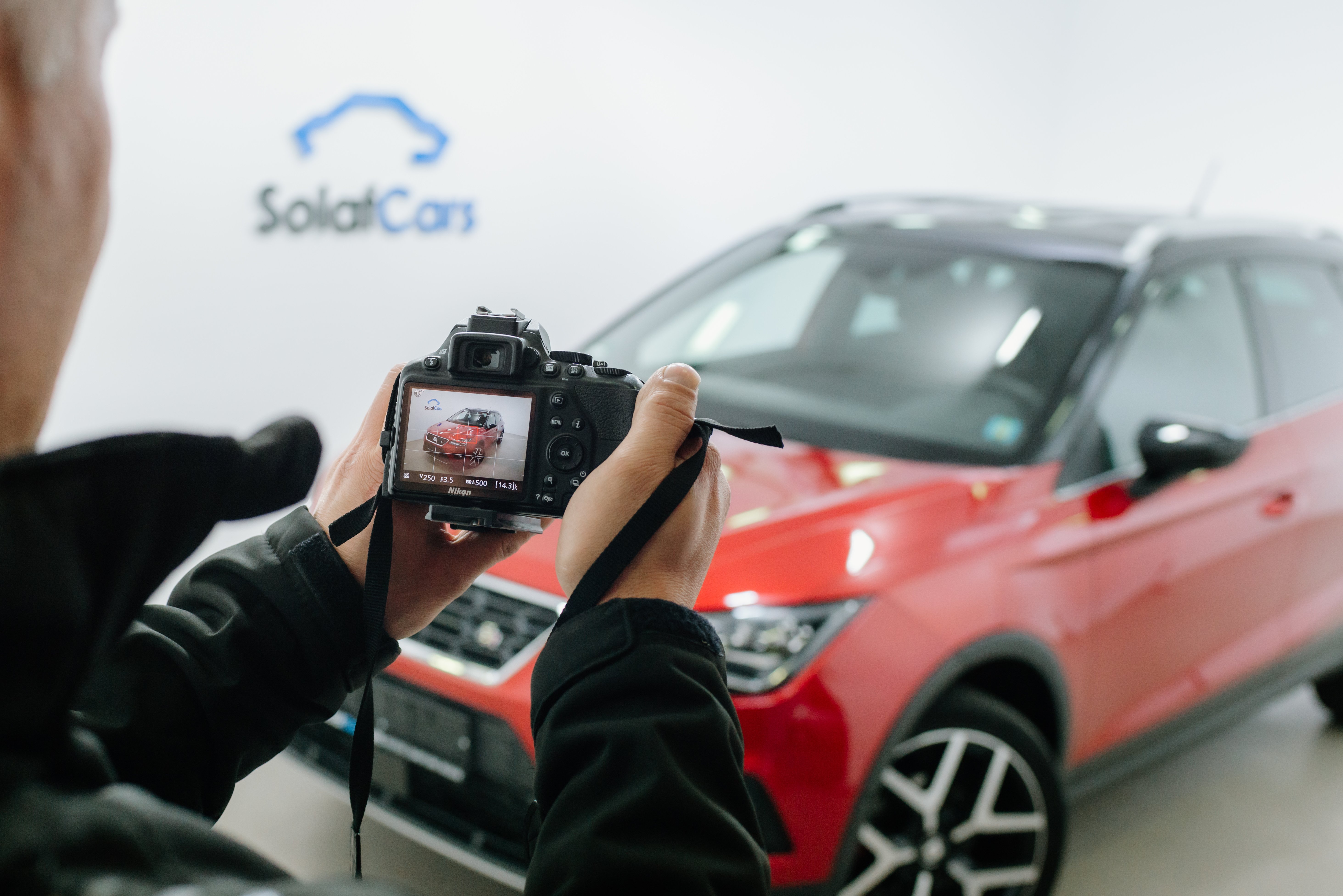Zbliżenie mężczyzny robiącego zdjęcie aparatem dslr czerwonego samochodu w studiu fotograficznym